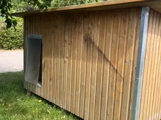Solidt udendørs hundehus i træ med fladt tag.