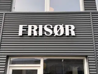 Frisørskilt i hvide bogstaver til facade