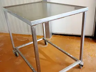 Rustfrit stål bord med vulstkant og hjul.